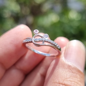May include: A silver ring with a unique design, featuring small clear stones and a decorative element. The ring is held in a hand, with the brand name "Ankit Diamond Jewels" visible at the bottom.