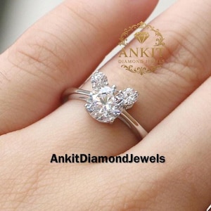 May include: A silver ring with a large, round, clear diamond center stone and two smaller diamonds on either side, forming a Mickey Mouse-like shape. The ring is on a finger. The text "AnkitDiamondJewels" is at the bottom.