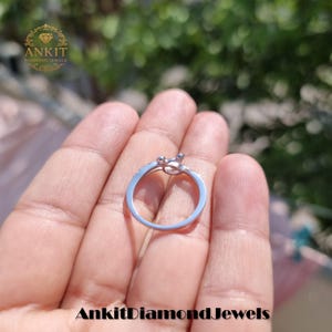 May include: A silver ring with a knot design, featuring small, sparkling stones. The ring is held in a hand, with the brand name "Ankit Diamond Jewels" visible at the bottom. The ring is a piece of jewelry.