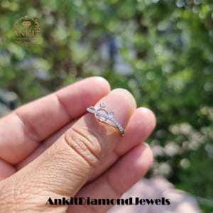 May include: A delicate silver ring with a unique design, featuring small diamonds and a distinctive shape. The ring is set with multiple small, clear gemstones. The ring is a piece of jewelry.