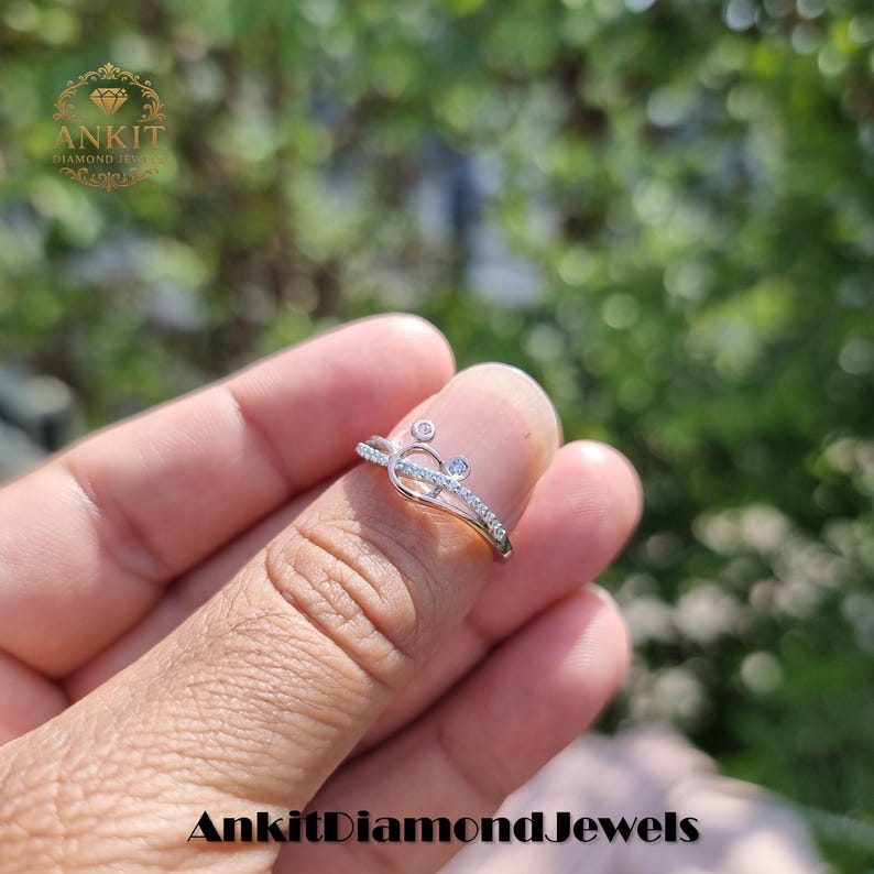 May include: A delicate silver ring with a unique design, featuring small diamonds and a distinctive shape. The ring is set with multiple small, clear gemstones. The ring is a piece of jewelry.