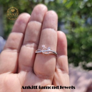 May include: A rose gold ring with a unique design, featuring small diamonds. The ring has a delicate, curved shape with a cluster of stones at the top. The brand name "Ankit Diamond Jewels" is visible in the image.
