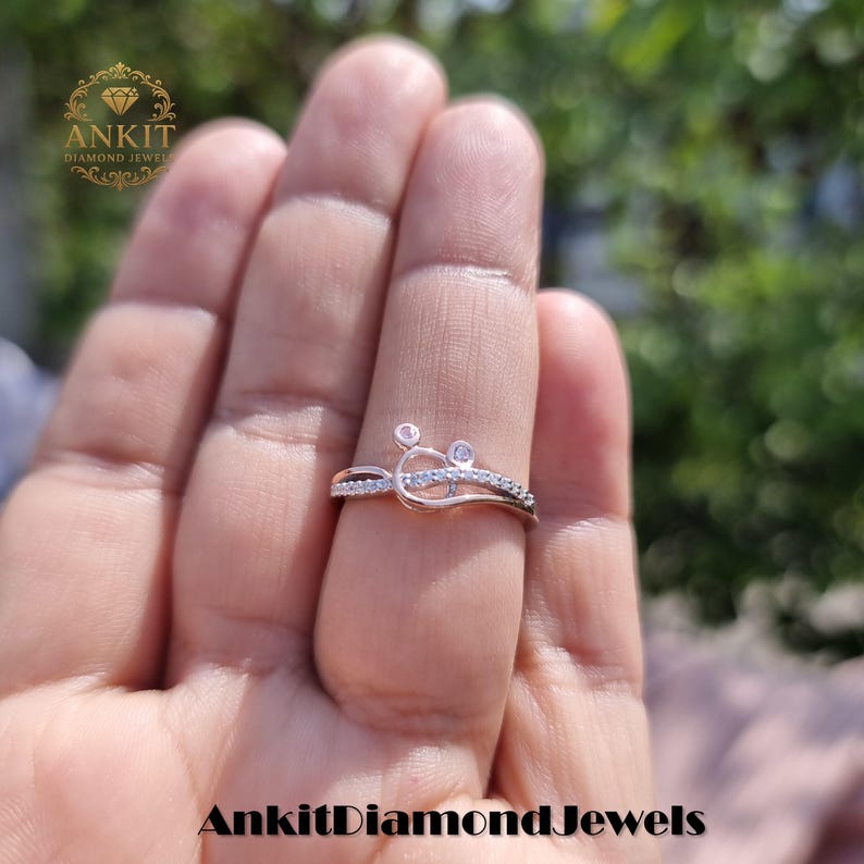 May include: A rose gold ring with a unique design, featuring small diamonds. The ring has a delicate, curved shape with a cluster of stones at the top. The brand name "Ankit Diamond Jewels" is visible in the image.
