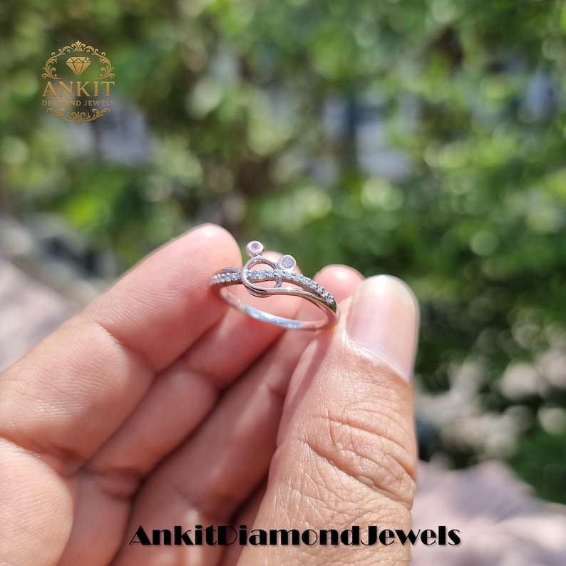 May include: A silver ring with a unique design, featuring small clear stones and a decorative element. The ring is held in a hand, with the brand name "Ankit Diamond Jewels" visible at the bottom.