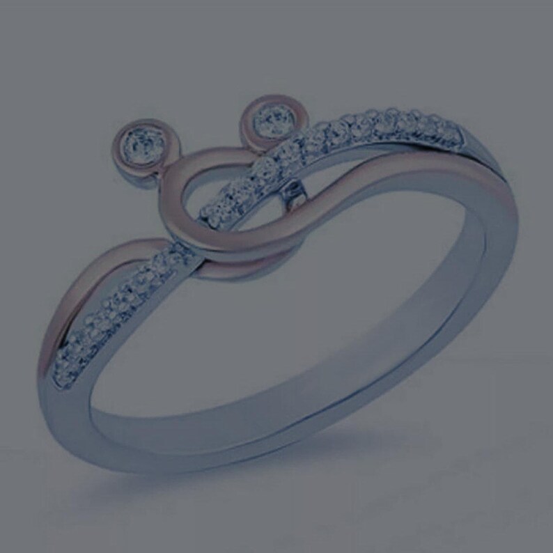 May include: A silver-toned ring with a unique design. The ring features a swirling, looping pattern with small, sparkling stones set along the curves. Two circular accents are at the top of the ring.