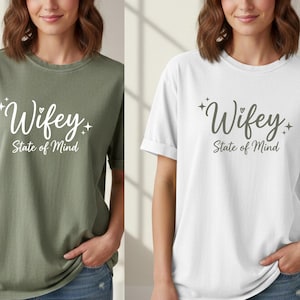 Könnte beinhalten: Zwei T-Shirts, eines olivgrün und eines weiß, jeweils mit dem Wort "Wifey" in Schreibschrift und dem Satz "State of Mind" darunter. Die Shirts sind kurzärmelig und haben eine lockere Passform. Das Bild enthält auch ein Logo und die Worte "DIGITAL DOWNLOD".