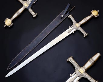 May include: A silver-toned sword with a gold-colored pommel and crossguard featuring intricate engravings, accompanied by a black leather scabbard with a strap. Two additional sword hilts with matching ornate metalwork are also displayed.