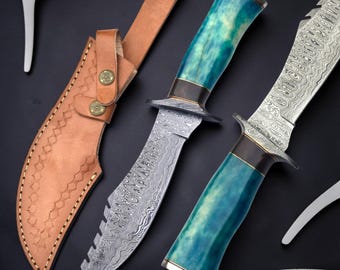 May include: Two fixed-blade knives with patterned Damascus steel blades and teal marbled resin handles, featuring dark metal bolsters. A tan leather sheath with decorative stitching and two brass-colored snap buttons is included.