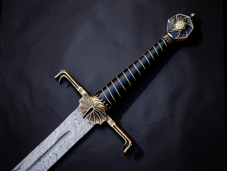 Op de afbeelding: Een zwaard met een patroon van Damascusstaal en een messing stootplaat met een waaiervormig midden. Het handvat is omwikkeld met zwart materiaal met gouden draadaccenten, bekroond met een zeshoekige pommel met een zonnestraal-embleem.