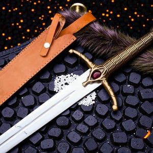 May include: A decorative sword with a gold-colored handle and a silver blade, featuring a red gem on the hilt. The sword rests beside a brown leather sheath and a fur accent. The background is a dark surface with scattered orange lights.
