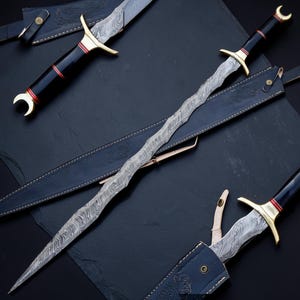 May include: A wavy-bladed sword with a Damascus steel pattern, featuring a black handle with red accents, a brass crossguard, and a crescent-shaped pommel. The sword is accompanied by a black leather sheath with embossed floral details.