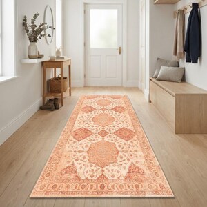 May include: A long rectangular runner rug featuring a repeating medallion pattern in shades of terracotta orange and cream. The rug has a detailed floral border and a distressed finish, covering the floor in a hallway with light wood flooring.