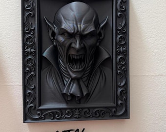 May include: A black 3D-printed relief of a vampire's face, framed in a decorative black border. The vampire is depicted with an open mouth, sharp teeth, and pointed ears. Text at the bottom reads "DIGITAL FILE for 3d printing."