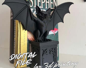 May include: A black bat ornament with spread wings, standing on a decorative plinth. The ornament is in front of a book with the name "Stephen King" visible. The text "DIGITAL FILE for 3d printing" is also present.
