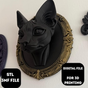May include: A black cat head sculpture with large ears, mounted on a black oval plaque with a gold-coloured ornate frame. The image includes text that reads "DIGITAL FILE FOR 3D PRINTING" and "STL 3MF FILE".