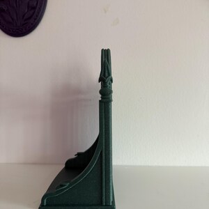 Peut inclure: Une &eacute;tag&egrave;re vert fonc&eacute; orn&eacute;e avec un dessus d&eacute;coratif. L'&eacute;tag&egrave;re a un design incurv&eacute; et est faite d'un mat&eacute;riau solide. L'&eacute;tag&egrave;re est con&ccedil;ue pour &ecirc;tre mont&eacute;e sur un mur et est probablement utilis&eacute;e pour afficher de petits objets.