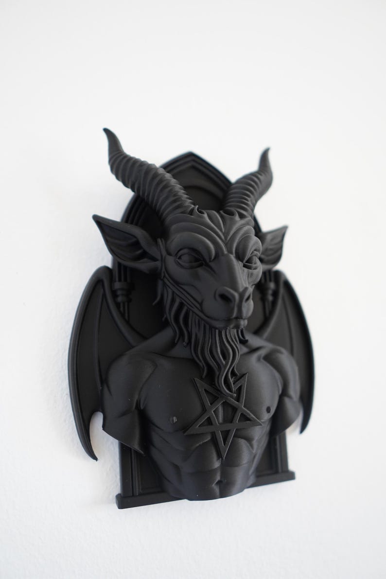 May include: A black wall sculpture of Baphomet, a goat-headed figure with horns, wings, and a pentagram on its chest. The sculpture is mounted on a wall and has a detailed, three-dimensional design. The sculpture is a gothic or occult-themed decorative item.