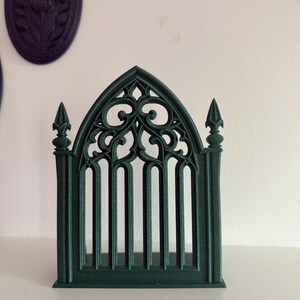 Peut inclure: Une fen&ecirc;tre ou porte d&eacute;corative de style gothique vert fonc&eacute;. Le design complexe pr&eacute;sente des arcs bris&eacute;s, des barres verticales et des volutes orn&eacute;es. Il s'agit probablement d'un &eacute;l&eacute;ment d&eacute;coratif pour la d&eacute;coration int&eacute;rieure ou les projets d'artisanat.