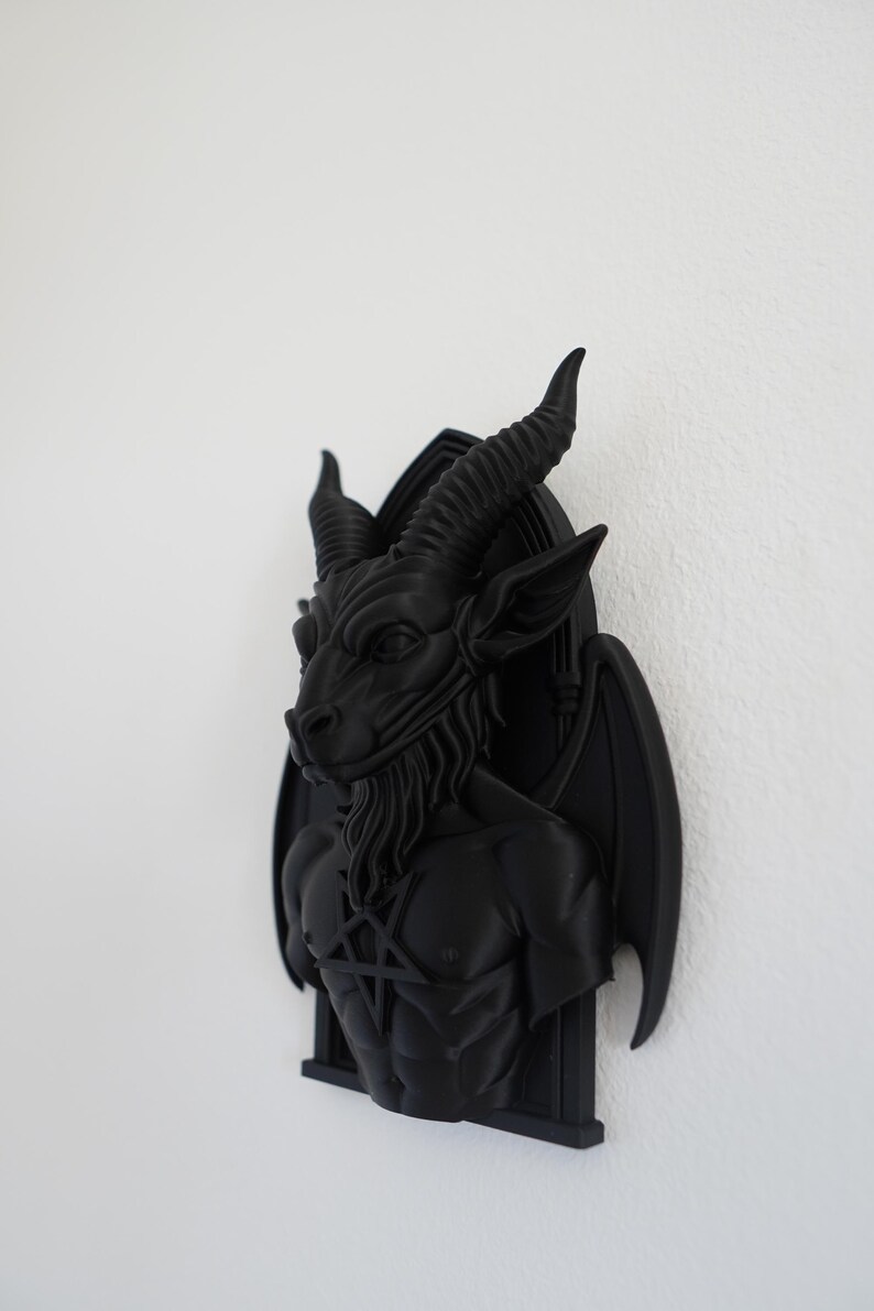May include: A black wall sculpture of Baphomet, a goat-headed deity, with large horns, a beard, and a pentagram on its chest. The sculpture has bat-like wings and is mounted on a black frame. The artwork is a gothic or occult-themed decorative item.