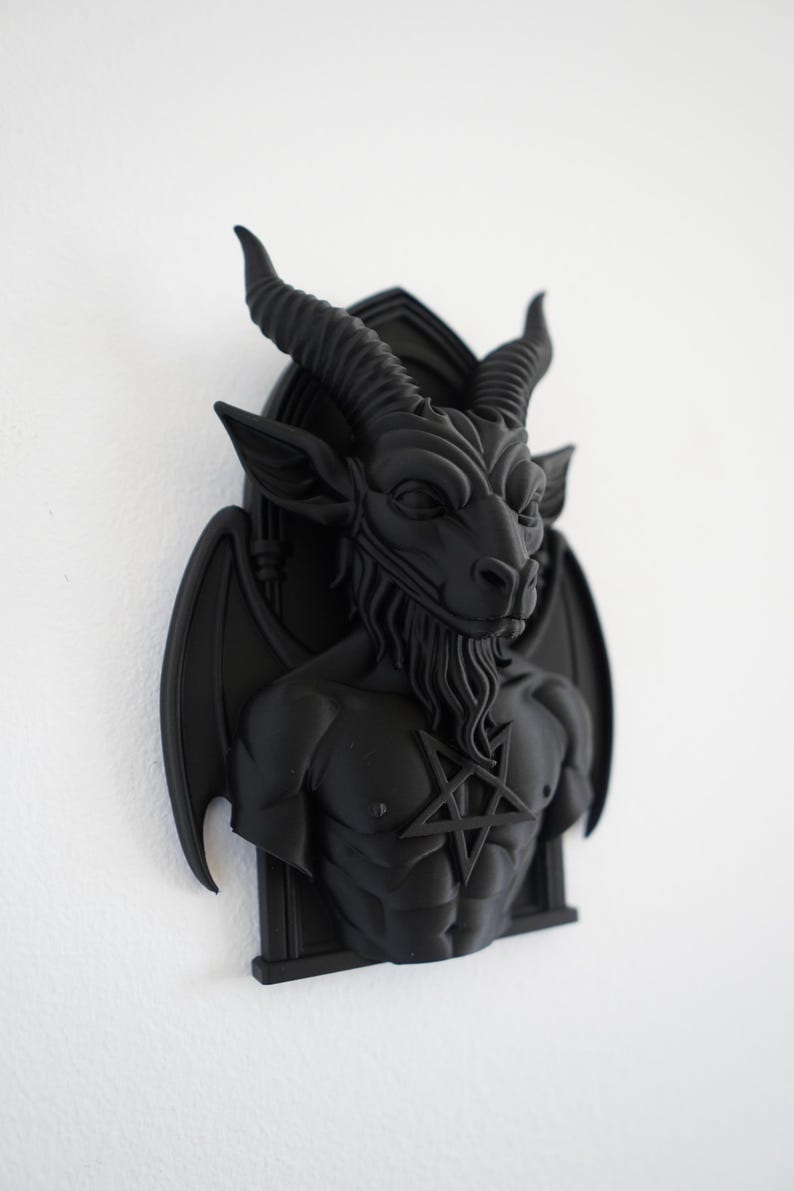 May include: A black wall sculpture of Baphomet, a goat-headed figure with horns, wings, and a pentagram on its chest. The sculpture is mounted on a white wall, showcasing the detailed features of the dark artwork.