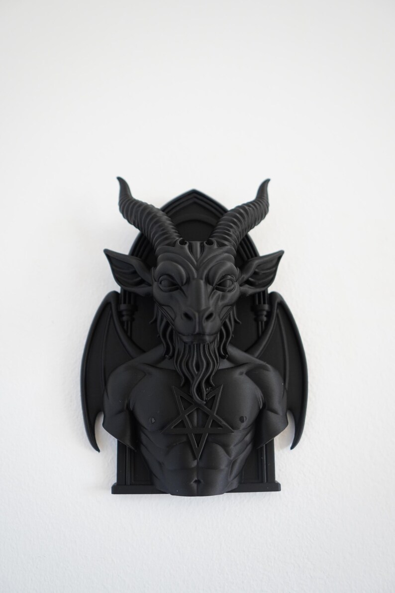May include: A black wall sculpture depicting Baphomet, a goat-headed deity, with a pentagram on its chest. The sculpture features detailed horns, a beard, and wings, mounted on a gothic-style frame. The artwork is a dark, gothic-themed decorative piece.