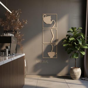 Può includere: Un set di tre decorazioni da parete in legno chiaro con un design ritagliato che mostra una teiera nel quadrato superiore, un flusso continuo di liquido nel quadrato centrale e una tazza da tè nel quadrato inferiore, con la scritta NATURAL.