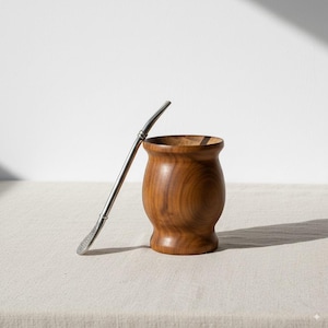 Peut inclure: Un récipient en bois pour yerba maté avec une paille bombilla en acier inoxydable. Le récipient est de couleur marron chaud, de forme arrondie et avec un bord évasé. La bombilla est argentée.