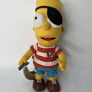 Puede incluir: Muñeco de peluche de Bart Simpson disfrazado de pirata. El muñeco tiene piel amarilla, un parche negro en el ojo y una camisa a rayas rojas y blancas. Sostiene una espada de juguete y lleva pantalones cortos azules y zapatos marrones.