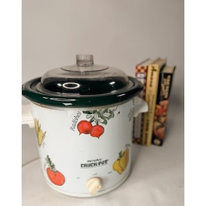 May include: A white Rival Crock-Pot slow cooker with a dark green rim and a clear glass lid. The exterior features colorful illustrations of vegetables including radishes and peppers, with the text Radishes printed near the radish graphic.