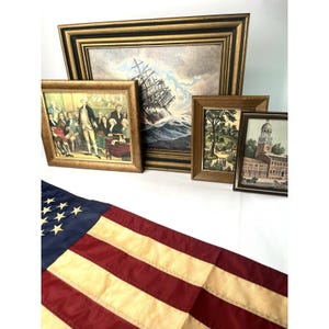 May include: A selection of framed vintage prints, featuring a ship at sea, a historical scene with figures, a landscape, and a building with a steeple. The frames are gold-toned, with an American flag in the foreground.