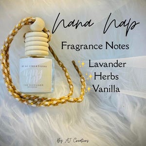 May include: A glass car diffuser bottle with a light wood cap and a braided gold and white cord. The label reads "hana hap", "BY AJ CREATIONS", and "CAR DIFFUSER". Text lists fragrance notes as "Lavander", "Herbs", and "Vanilla".