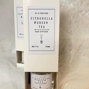 May include: Two white boxes containing a reed diffuser. The label states "Citronella & Green Tea Reed Diffuser" from "By AJ Creations". The diffuser is in a clear glass bottle, 50ml / 1.7 fl oz, and lasts 3-6 weeks.