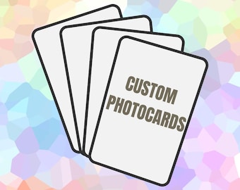 May include: A stack of four rectangular white cards with rounded corners and black borders. The top card features the text CUSTOM PHOTOCARDS in dark grey capital letters. The cards are arranged in a fan shape against a pastel mosaic background.