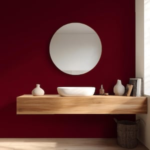 May include: A modern bathroom design featuring a round mirror above a wooden floating shelf. The shelf holds a white vessel sink, decorative vases, and books. The wall is a deep red color, and a woven basket sits below.