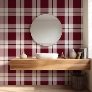 May include: A bathroom with a burgundy and white plaid wallpaper. A round mirror hangs above a wooden shelf with a white sink, decorative vases, and books. A woven basket sits below the shelf, and a window is on the right.