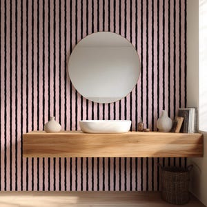 May include: A modern bathroom scene featuring a round mirror, a white vessel sink, and a wooden shelf. The backdrop is a pink wall with vertical black stripes. Decorative vases and books add to the aesthetic. A woven basket sits below the shelf.