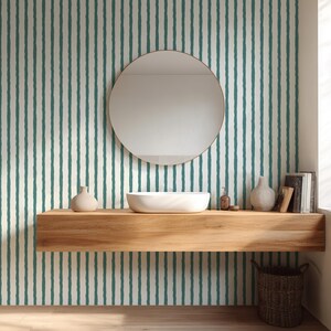May include: A modern bathroom with a round mirror, a white vessel sink, and a wooden shelf. The wall features a cream-colored background with vertical teal stripes. Decorative vases, a soap dispenser, and books are on the shelf. A woven basket sits below.