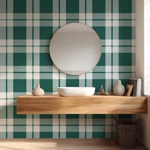 May include: A bathroom scene featuring a green and white plaid wallpaper. A round mirror hangs above a wooden shelf holding a white sink, vases, and books. A woven basket sits below the shelf, and a window is visible on the right.