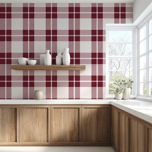 May include: A kitchen with a red and white plaid wallpaper design. The room features wooden cabinets, a wooden shelf with white vases and bowls, and a window with natural light.