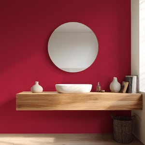 May include: A modern bathroom design featuring a round mirror, a white vessel sink, and a wooden floating shelf against a deep red wall. Decorative vases and books are arranged on the shelf, with a woven basket below.