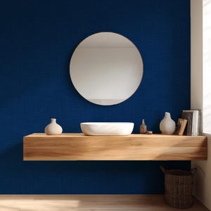 May include: A modern bathroom scene featuring a round mirror, a white vessel sink, and decorative vases on a wooden shelf. The shelf is mounted on a deep blue wall. A woven basket sits below.