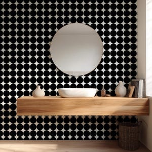 May include: A modern bathroom with a round mirror, a white sink, and a wooden shelf. The wall is decorated with a black and white polka dot pattern. Decorative vases and books are on the shelf, and a woven basket sits below.