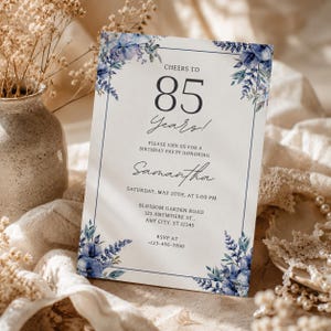 Peut inclure: Une carte d'invitation d'anniversaire rectangulaire ornée d'illustrations florales bleues dans les coins, avec le texte Cheers to 85 Years, Please join us for a birthday party honoring Samantha, Saturday, May 20th, at 5:00 PM, Blossom Garden Road.
