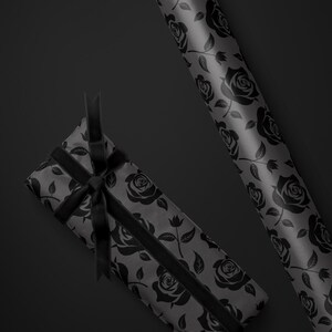 May include: A gift wrapped in gray paper with a black rose pattern, tied with a black ribbon. A roll of matching wrapping paper is also visible. The background is a solid black.
