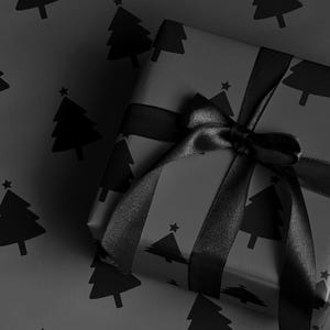 Pode incluir: Um presente embrulhado em papel de embrulho preto com um padr&atilde;o repetido de &aacute;rvores de Natal. O presente &eacute; amarrado com uma fita e la&ccedil;o de cetim preto. O fundo &eacute; o mesmo papel.