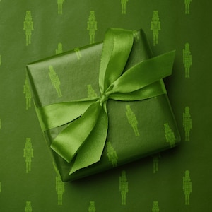 May include: A wrapped gift with a green satin ribbon bow. The gift is wrapped in green paper with a repeating pattern of nutcracker soldier figures. The background is the same green color with the same nutcracker pattern.