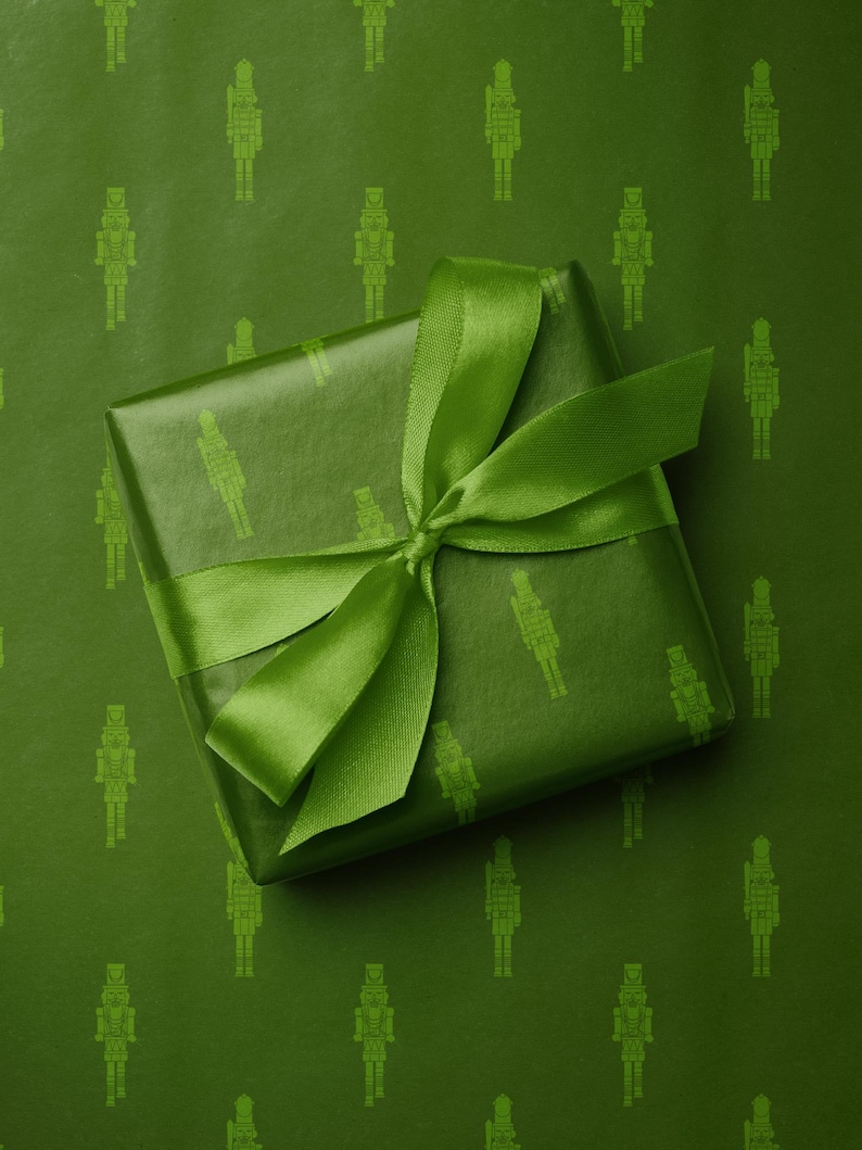 Op de afbeelding: Een ingepakt cadeau met een groene satijnen strik. Het cadeau is verpakt in groen papier met een herhalend patroon van notenkraker soldatenfiguren. De achtergrond is dezelfde groene kleur met hetzelfde notenkrakerpatroon.