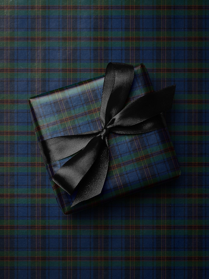 May include: A square gift wrapped in blue, green, and brown plaid paper, tied with a black satin ribbon. The ribbon is tied in a bow on top of the package. The gift is presented on a matching plaid background.