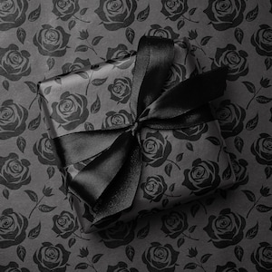 May include: A wrapped gift box with a black satin ribbon bow. The gift is wrapped in black paper with a rose pattern. The background is a matching black rose pattern.