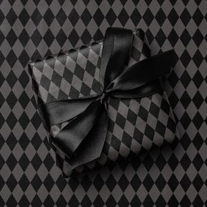 Peut inclure: Un cadeau emball&eacute; dans du papier &agrave; motifs de losanges noirs et gris, orn&eacute; d'un ruban de satin noir nou&eacute; en n&oelig;ud. Le cadeau est pos&eacute; sur un fond &agrave; motifs de losanges assortis.